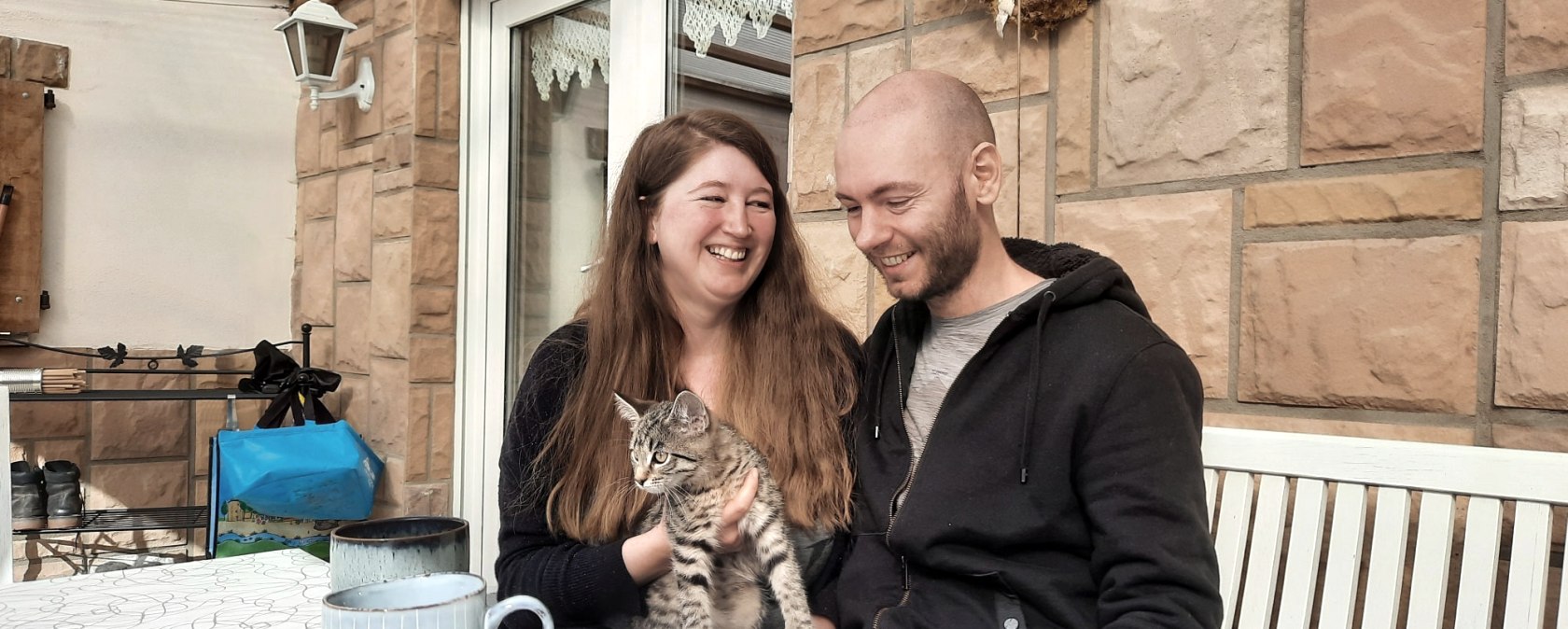 Julia und Helge mit Katze auf dem sonnigen Balkon, © Zukunftsinitiative Eifel