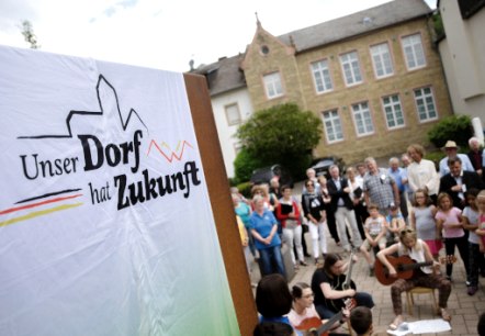 Bettingen im Bitburger Land ist mit aktuell 1.098 Einwohnern das gr&ouml;&szlig;te Dorf im Westen der Verbandsgemeinde mit Grundzentrumsfunktion. Der Ort verf&uuml;gt &uuml;ber eine sehr gute Infrastruktur: KiTA, Schule, Sportanlagen, B&uuml;rgerhalle, Jugendraum, Dienstleister, &Auml;rzte, Handel und Gewerbe, sowie Landwirtschaft und Gastronomie sind vorhanden. Im Ort besteht eine Pflegeeinrichtung mit 48 Pflegepl&auml;tzen. Leitsatz f&uuml;r Bettingen: Gute Infrastruktur erhalten und weiterentwickeln. Gemeinsam Altes bewahren und Neues wagen., &copy; BMEL/Photothek