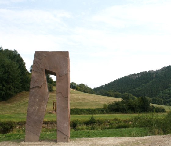 &bdquo;Br&uuml;ckenschlag&ldquo; hei&szlig;en die zwei Arbeiten von Christoph Mancke aus L&uuml;nebach. Er platzierte den offenen Sandsteinblock, ein stilisierter schreitender Mensch und seine st&auml;hlerne Verdoppelung, dies- und jenseits des Grenzflusses Our. Der Durchblick schafft die Verbindung., &copy; Eifel hautnah, Stefan Lieser