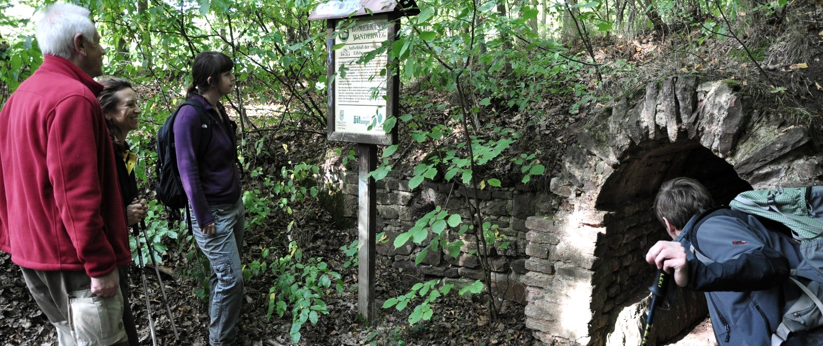 Vier Wanderer stehen vor einer Infotafel und einem alten Tunnel am R&ouml;merkanal-Wanderweg im Wald., &copy; Wandermagazin/ N. Glatter
